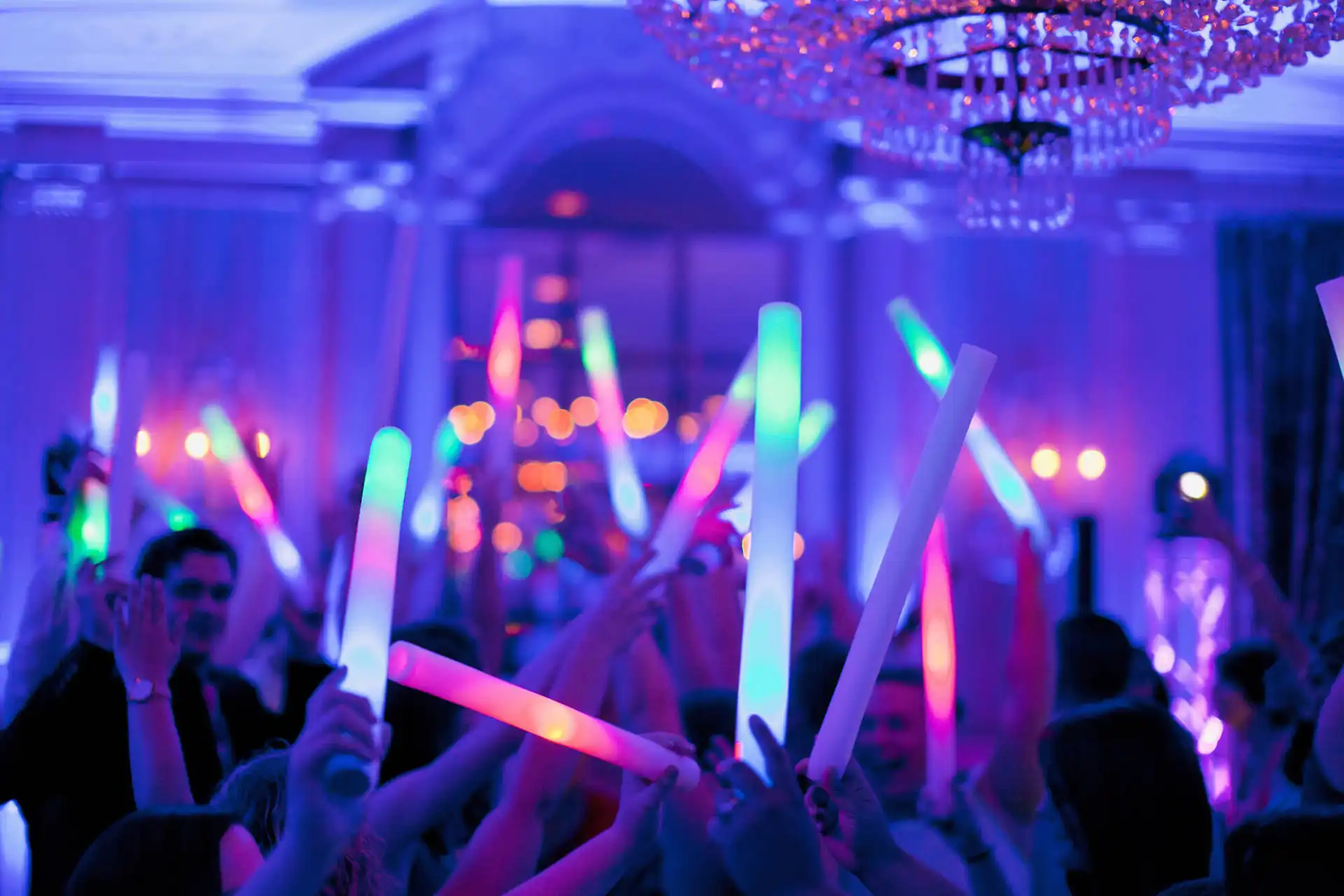 Partygäste mit Leuchtstäben unter bunten Scheinwerfern